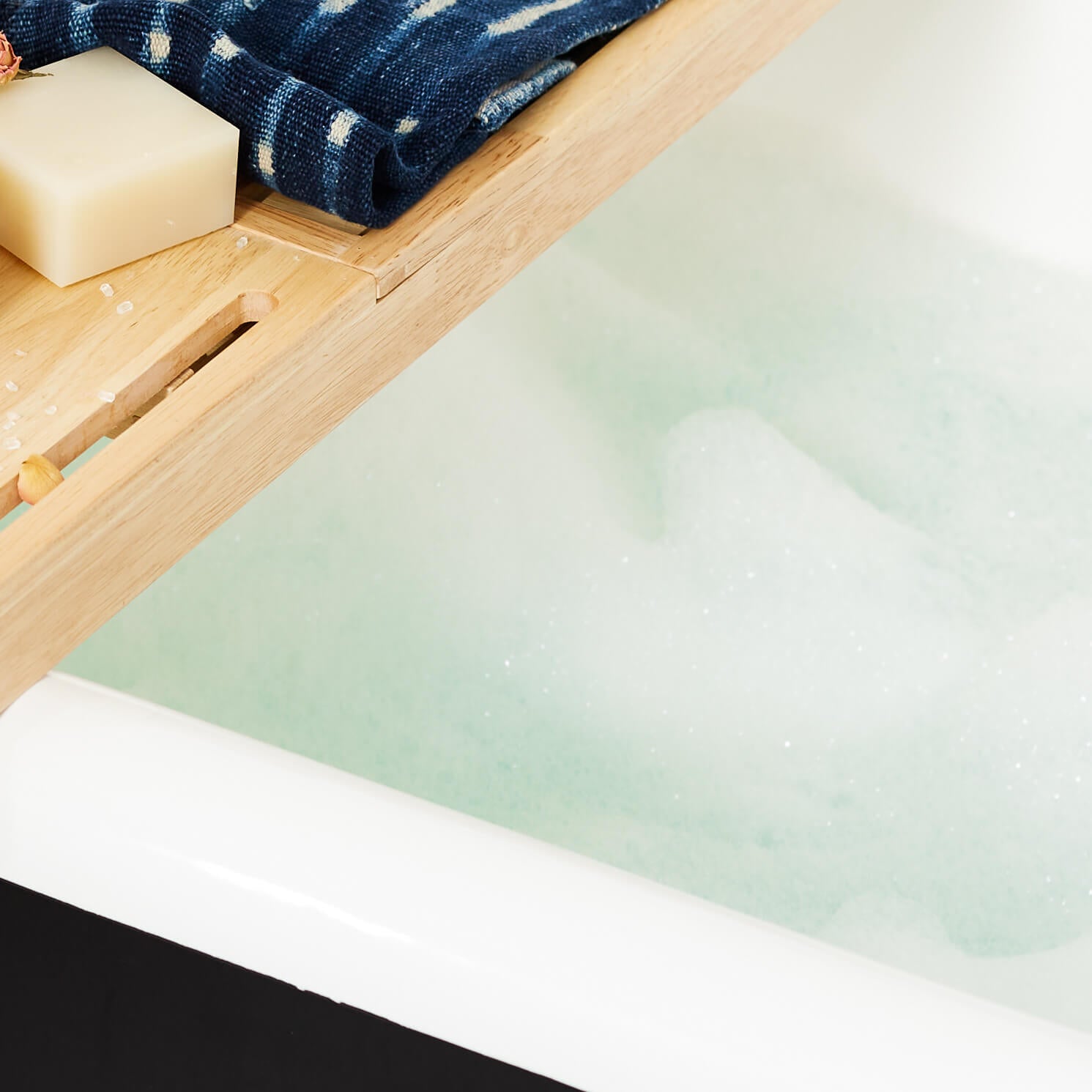 Bathing products, a towel and flowers on a board resting on a claw foot tub.