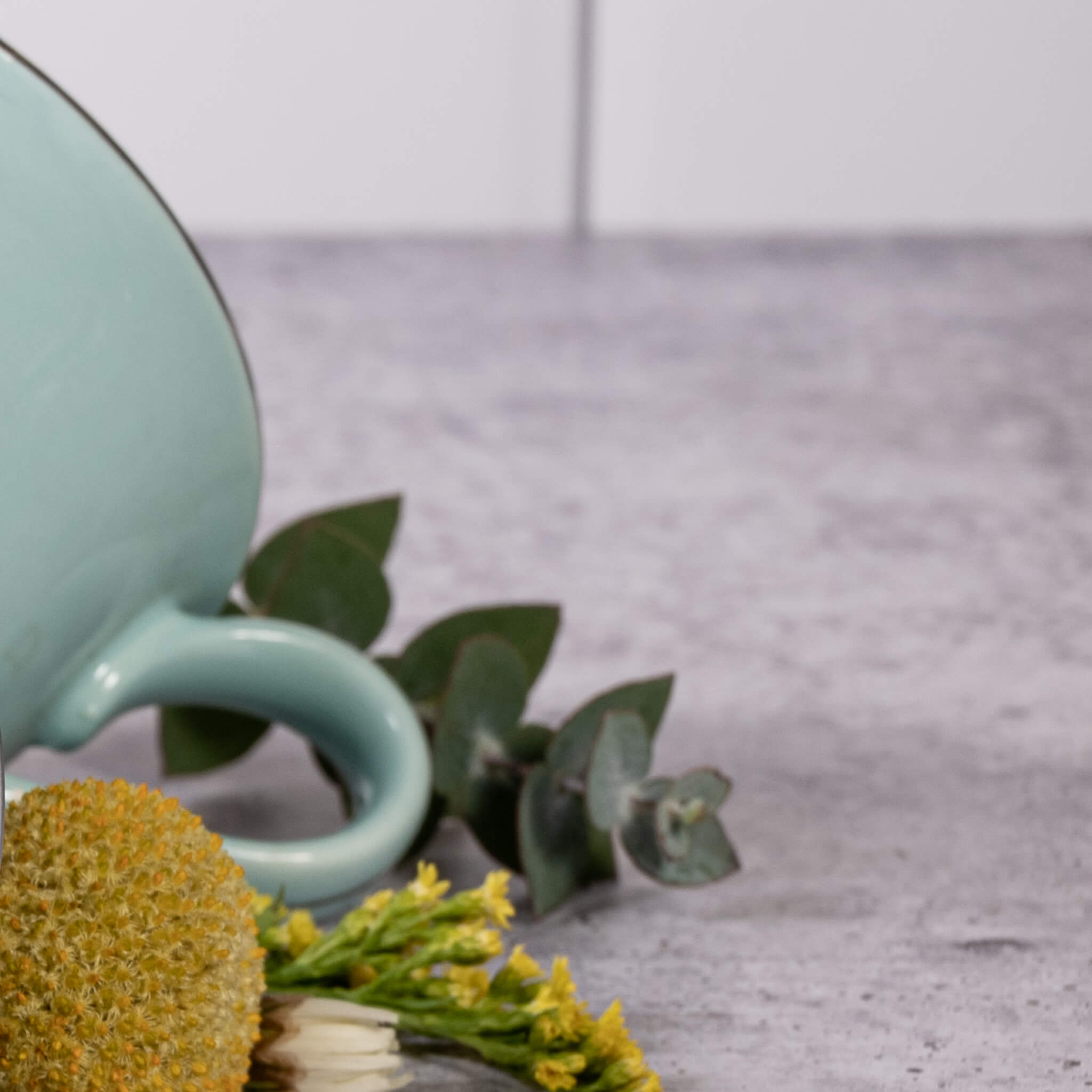 A turquoise mug and flowers on a concrete counter.