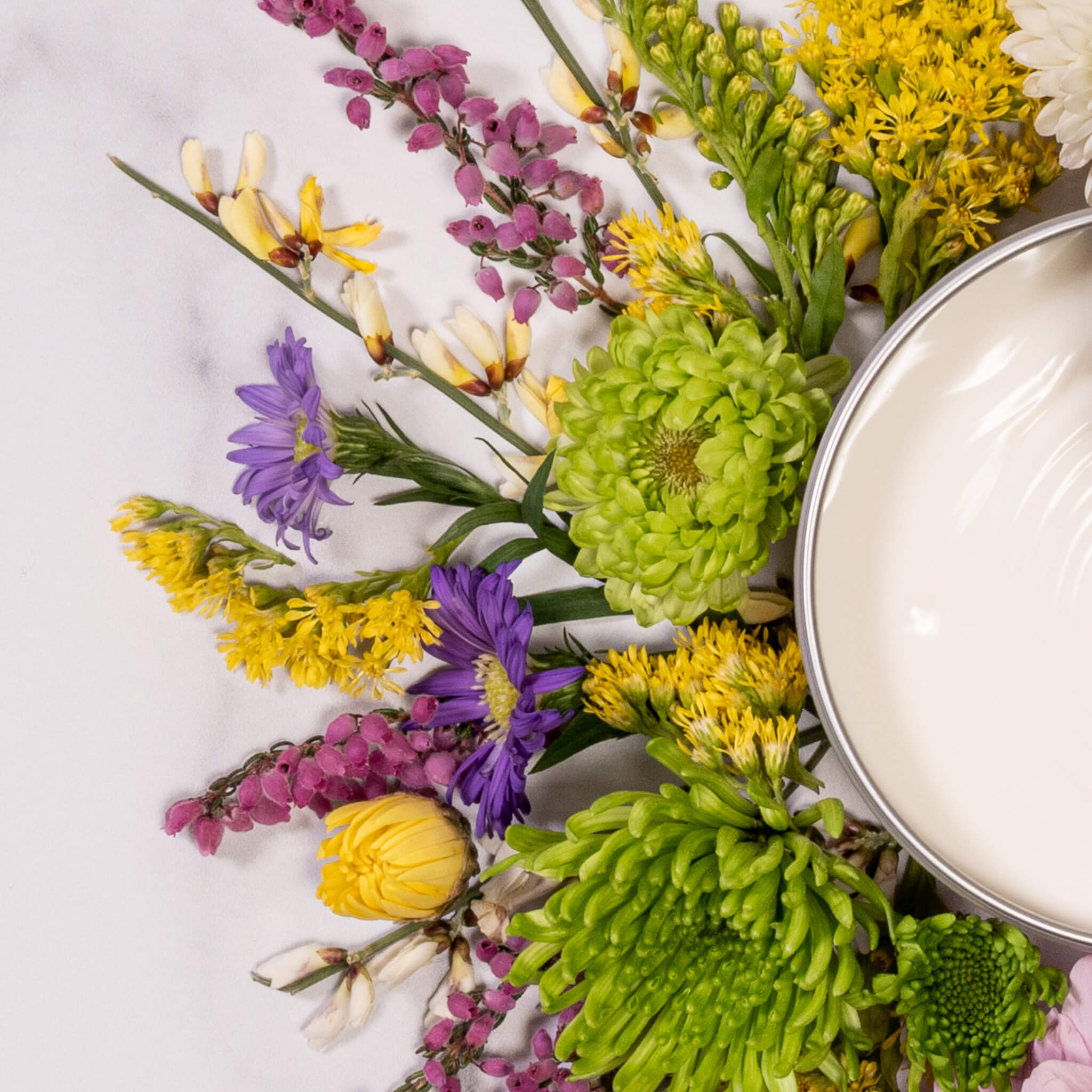 Tin of lemongrass hand & body cream nestled in a bouquet of colorful flowers. 