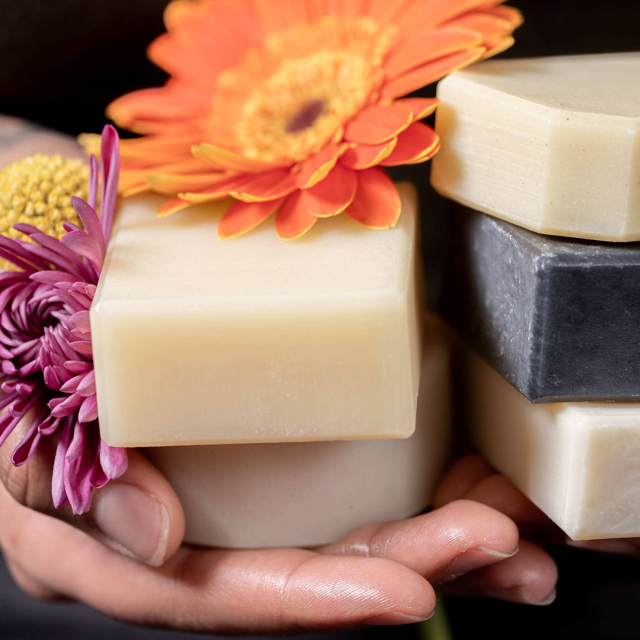 Tati holding 5 different bars of unboxed soap and some colorful flowers.