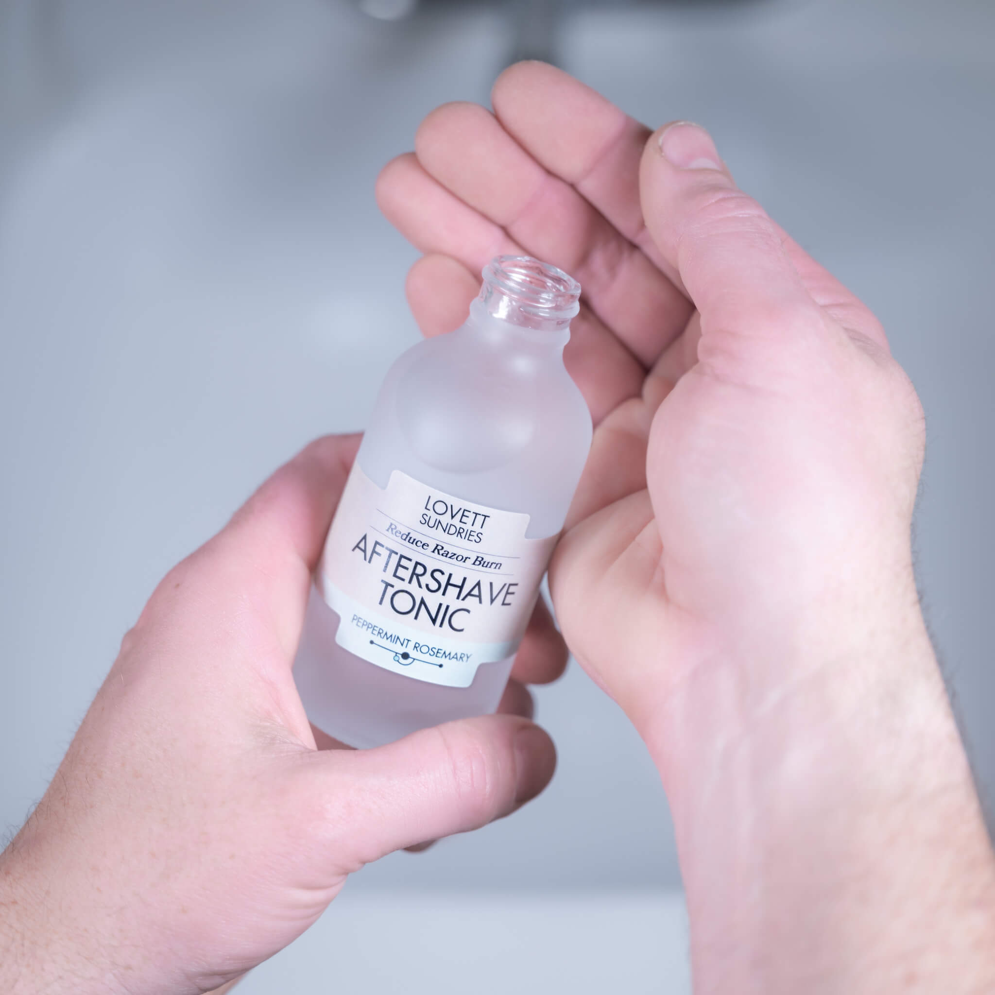 A person pouring all natural peppermint rosemary aftershave tonic into their hands over a sink. 