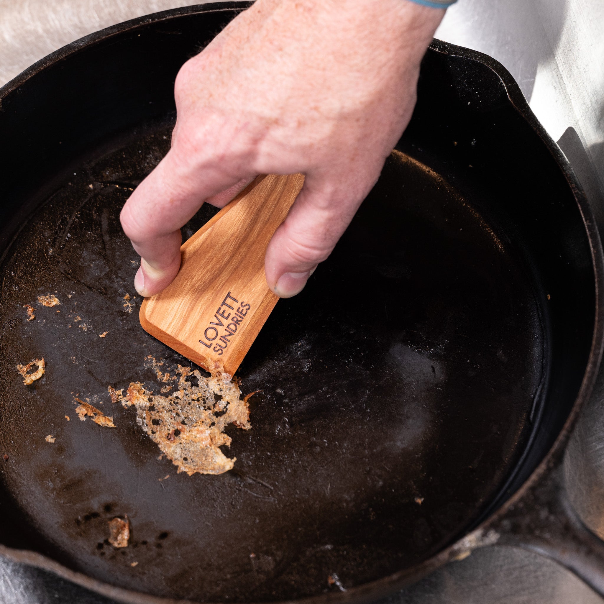 Jeff scraping food off of his cast iron skillet with his all natural hand made wooden scraper.