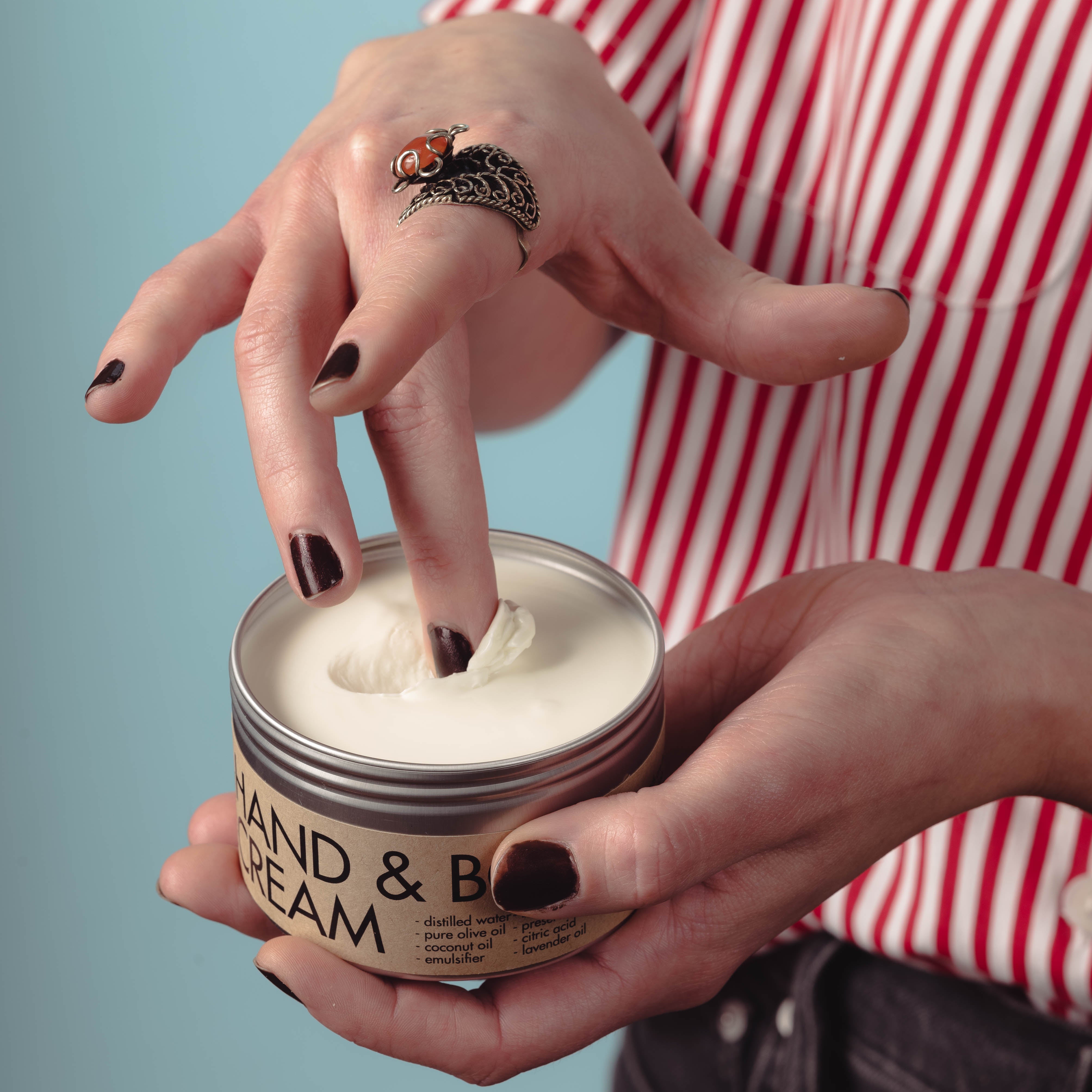 Megan dips a finger into a fresh tin of Hand & Body Cream, scooping out a dollop to use.
