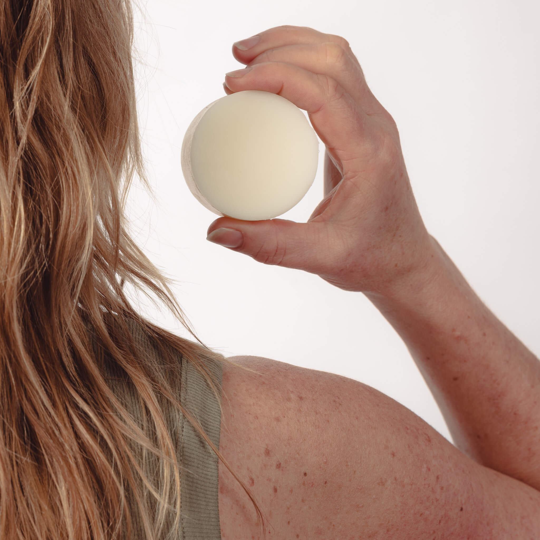 Marit holding a solid all-natural conditioner bar next to her hair. 