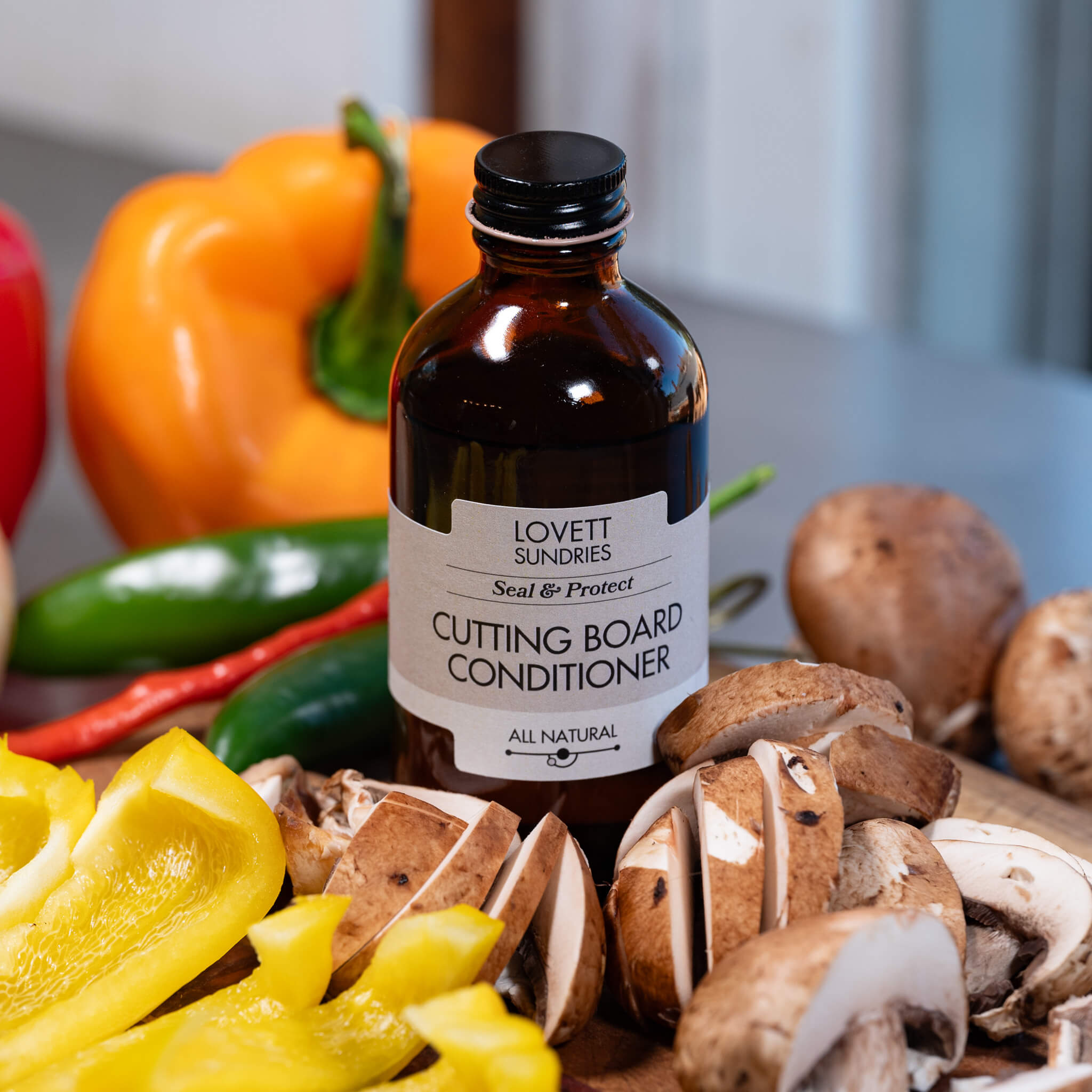 Brown glass bottle of all natural cuttingboard conditioning oil surrounded by chopped vegetables.