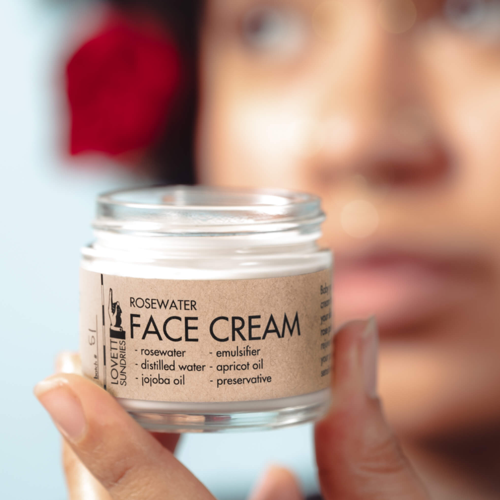 A person holding up a jar of rose face cream, made with rosewater.