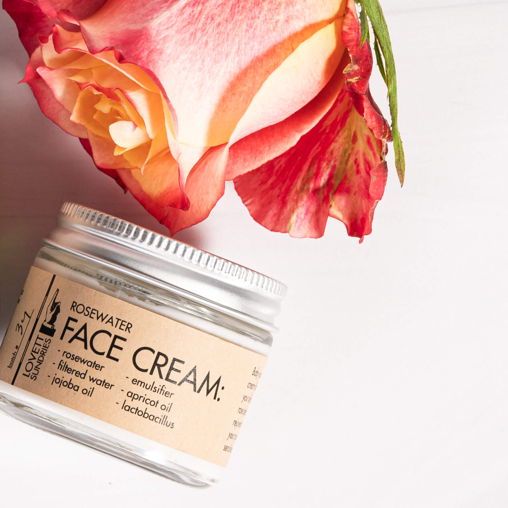 A jar of rosewater face cream next to a rose.