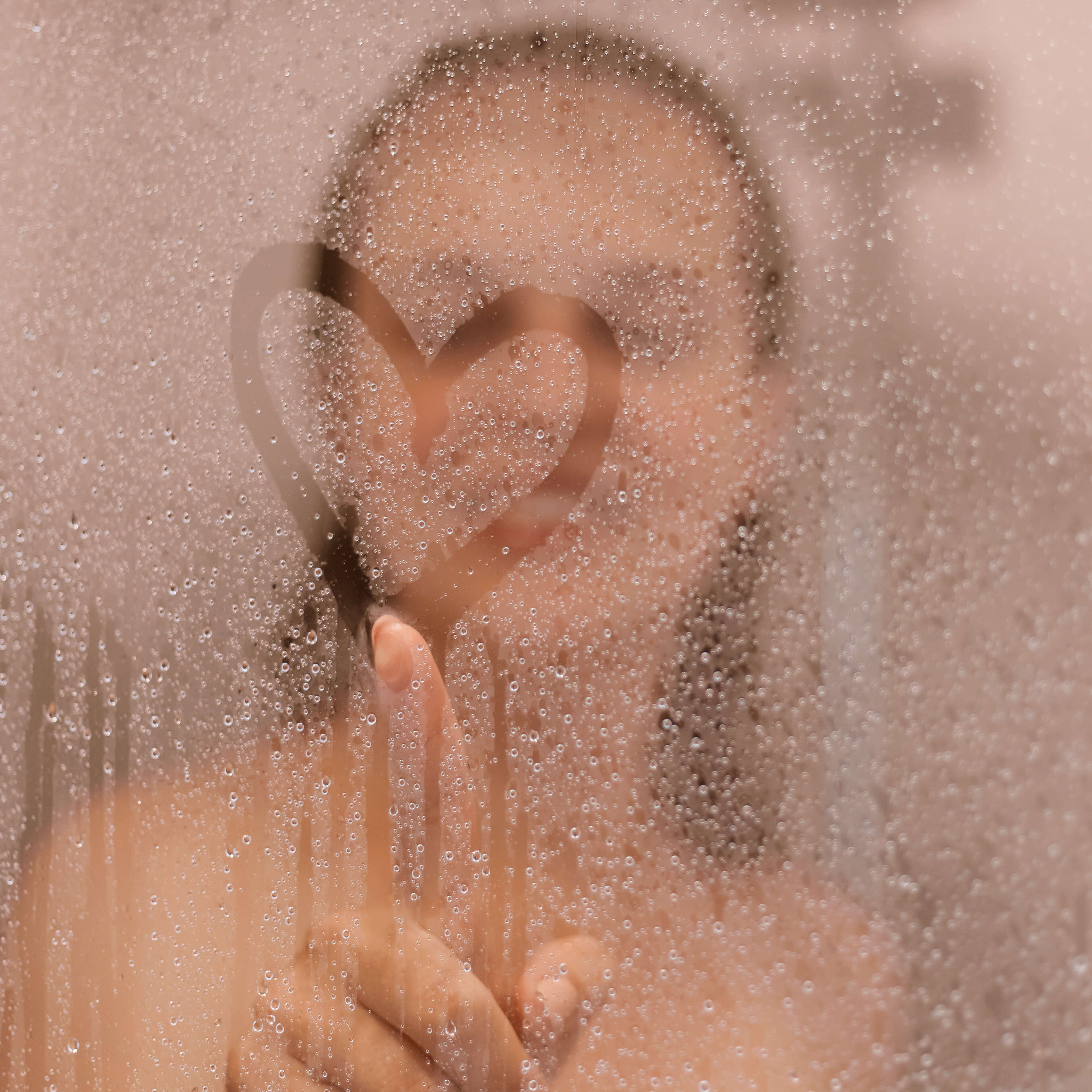 Woman drawing a heart on the glass of a steamy shower. 