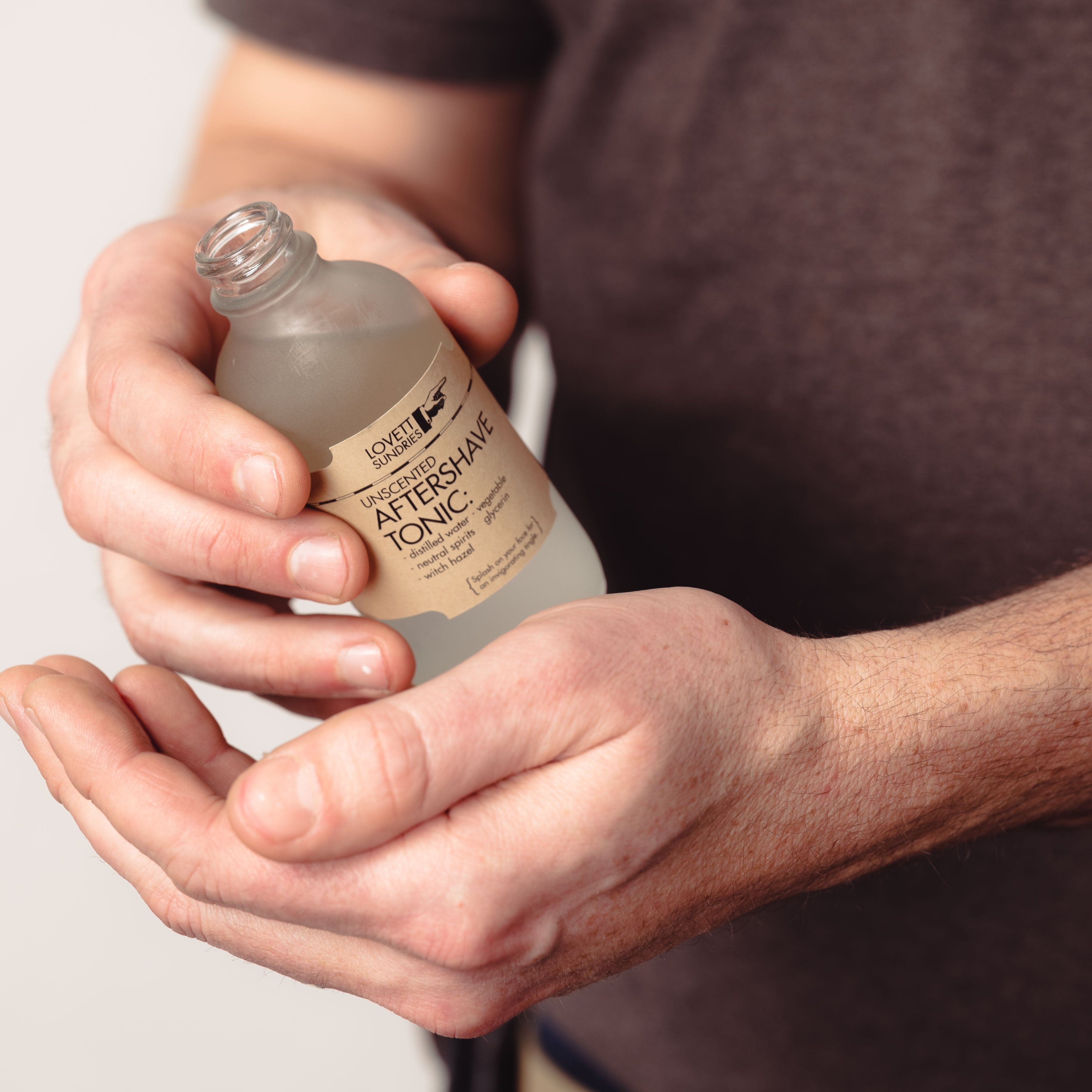A person holding a bottle of aftershave tonic.