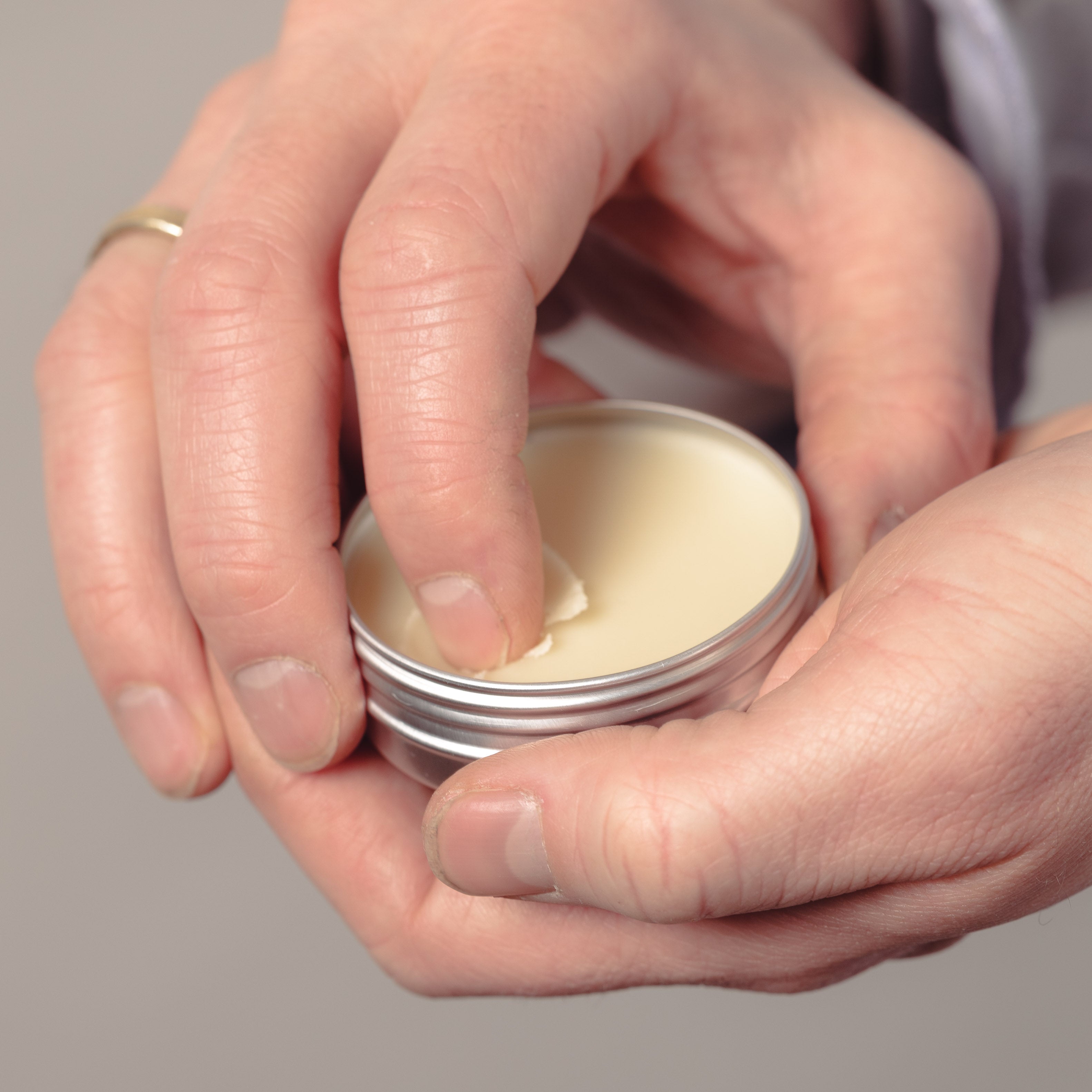 A person scooping out a little bit of beard balm from a tin. 