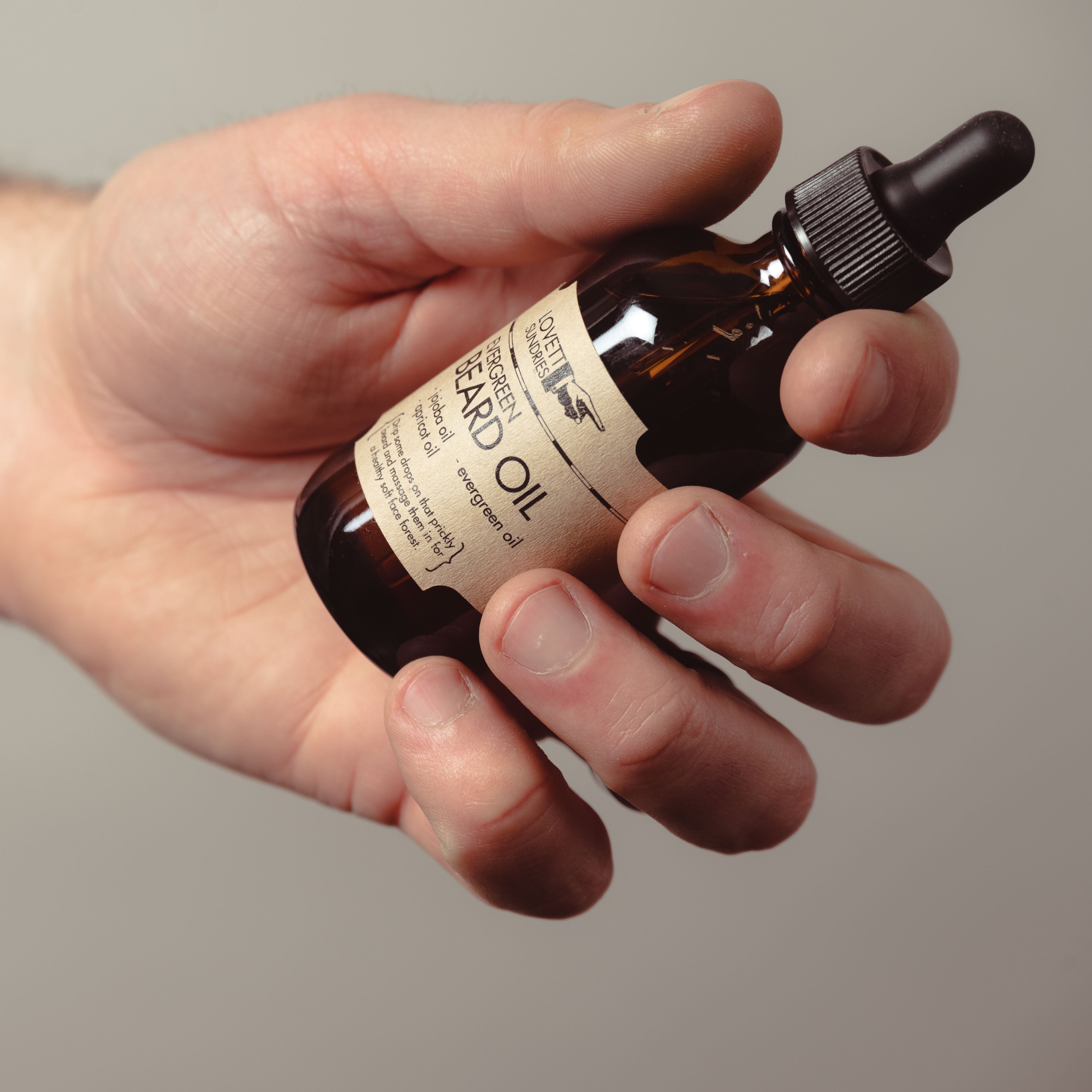 A bottle of Beard Oil is held comfortably in the grasp of a hand.