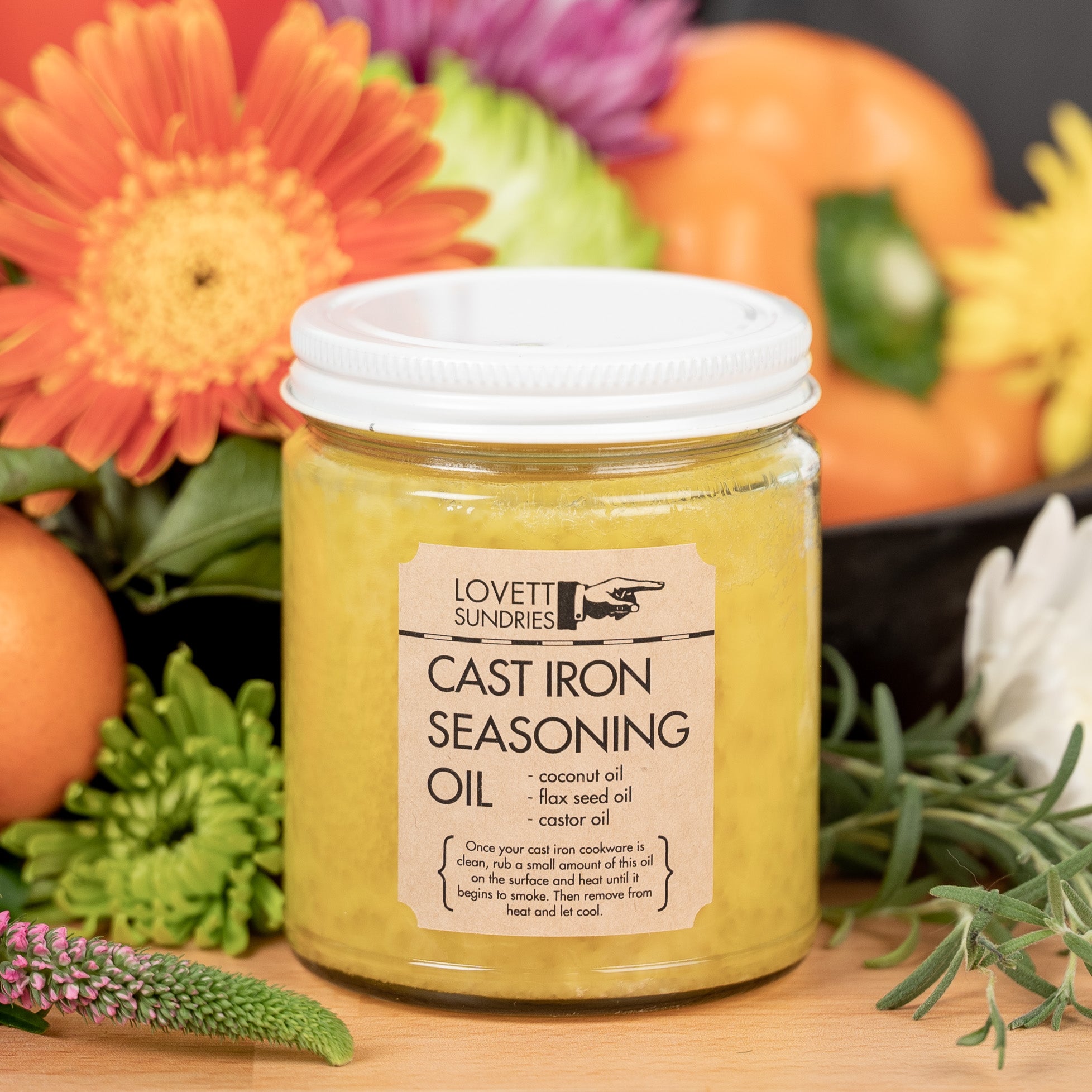 A glass jar of cast iron seasoning oil in a bed of flowers and vegetables on a kitchen counter. 