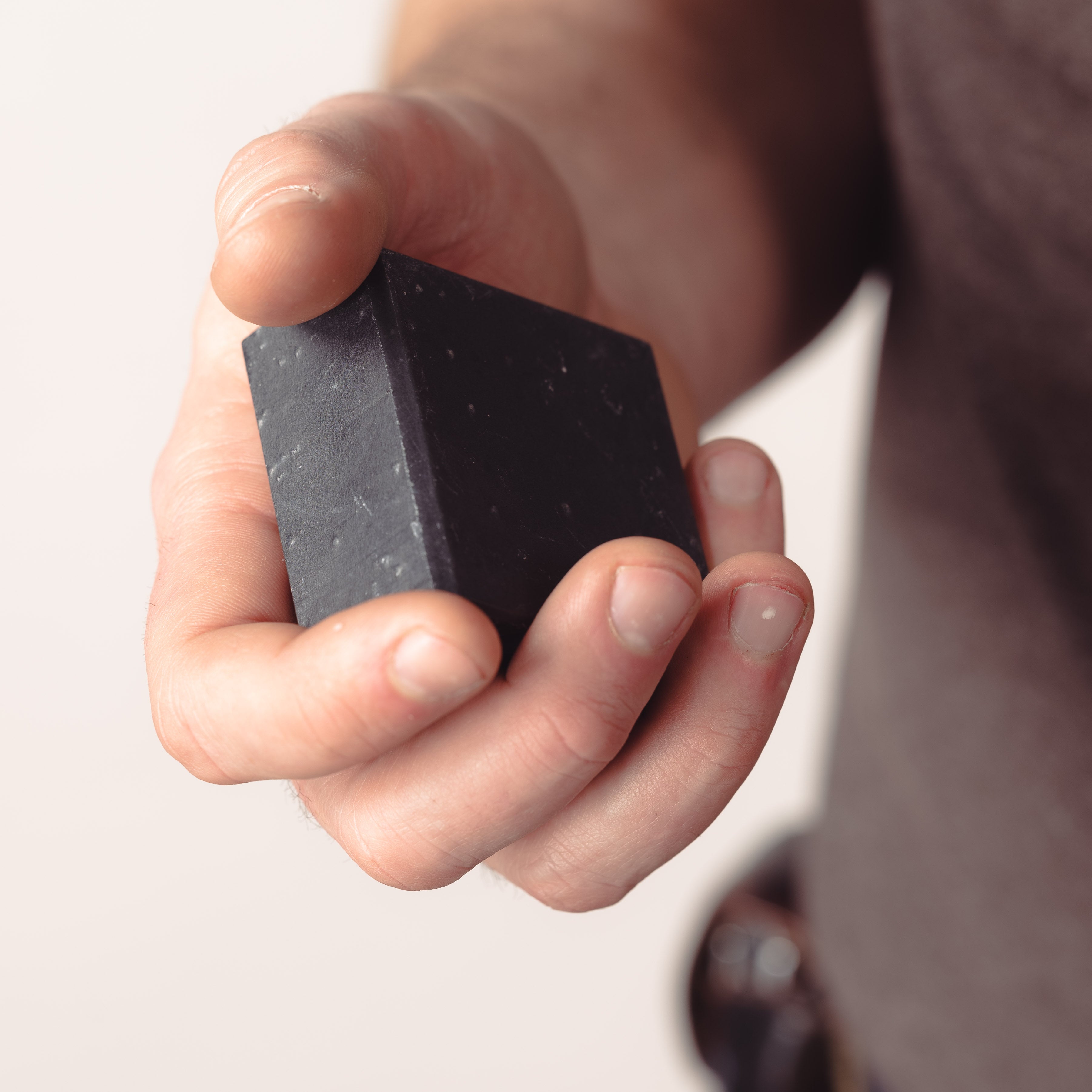 A person holding an all-natural clay and charcoal soap bar.