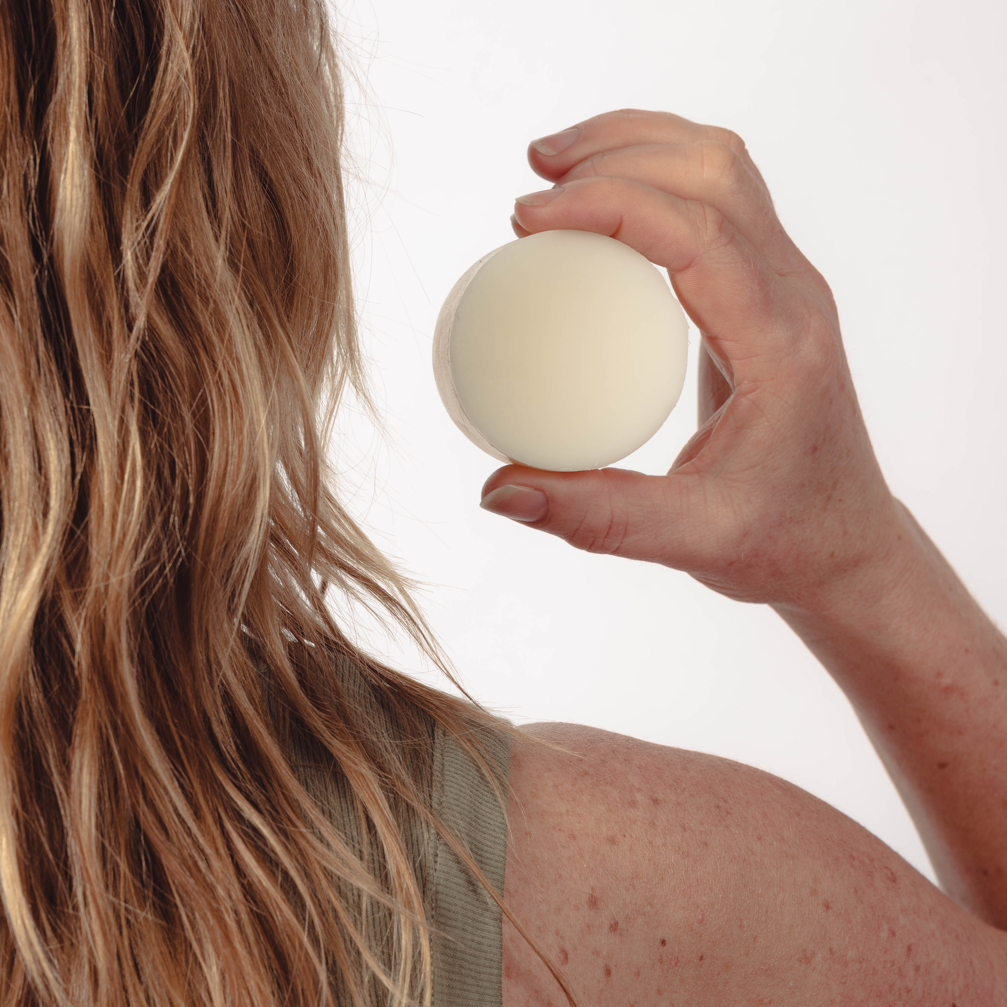 A woman with blonde hair and a bare shoulderholding up an all natural solid conditioner bar.