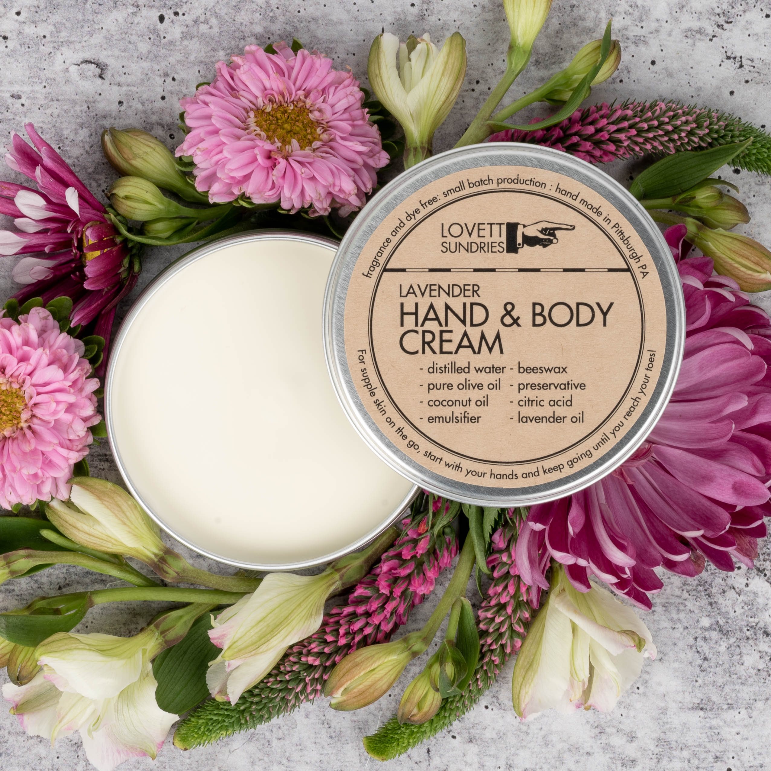Open Lavender Hand & Body Cream surrounded by fresh spring flowers.