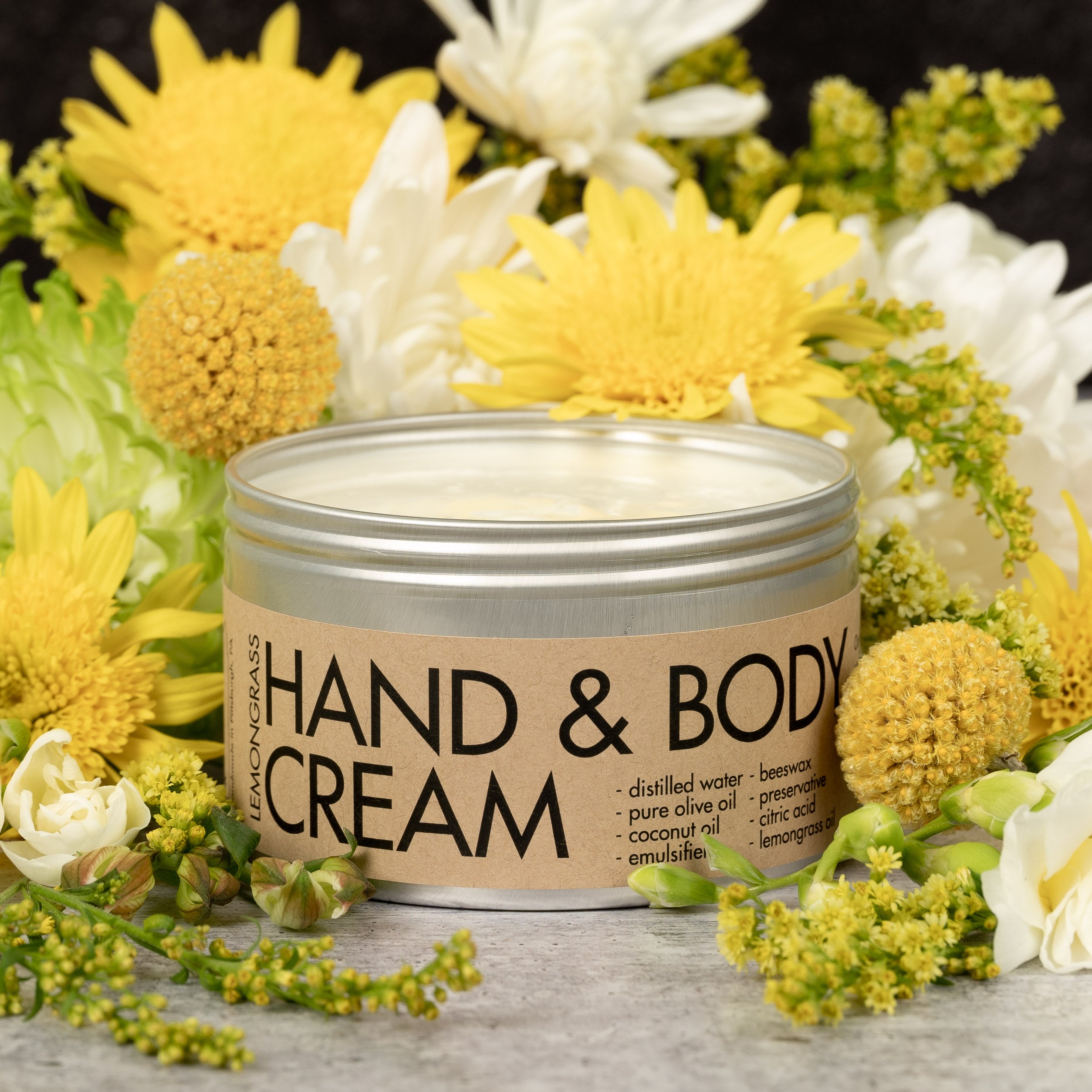 A container of Lemongrass Hand & Body cream next to flowers.