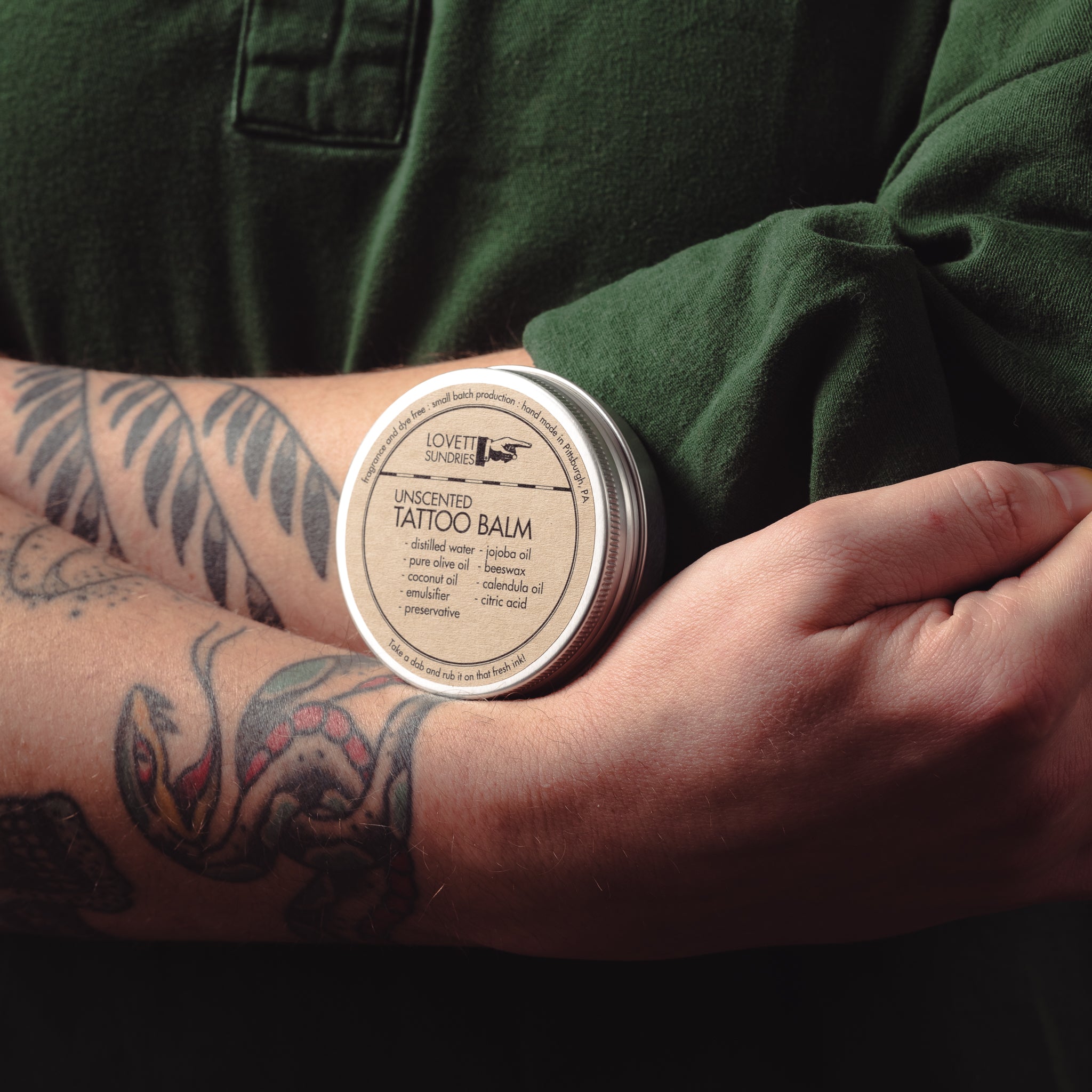 Tattooed arms holding a tin of all natural tattoo balm. 