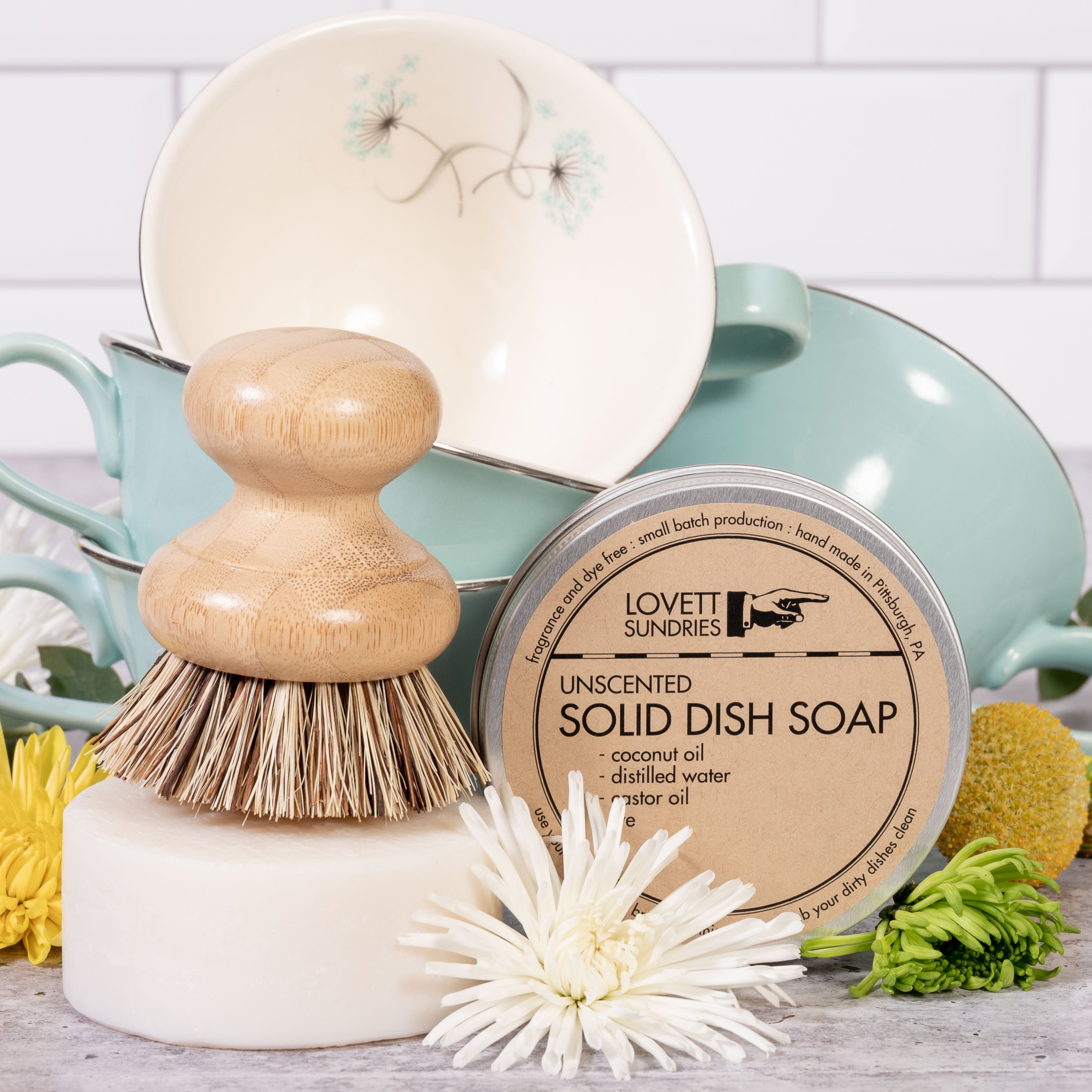 All Natural Dish Soap with a brush in front of vintage teal tea cups and flowers.
