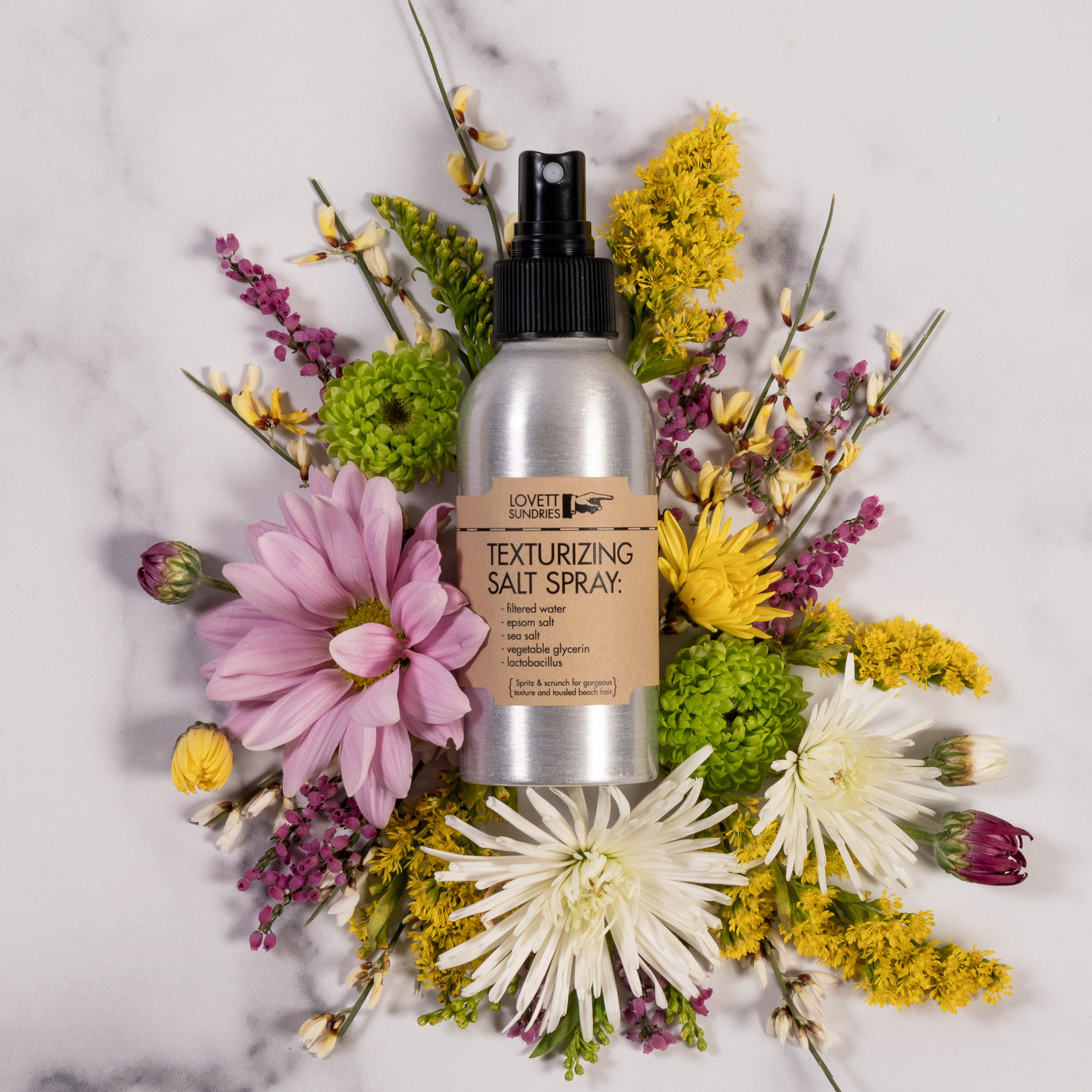All natural unscented texturizing salt hair spray for voume and hold in a recyclable aluminum bottle in a bed of flowers. 